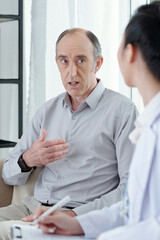 Senior man worrying about health talking to general practitioner visiting him at home