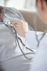 Close-up image of doctor putting chestpiece of stethoscope on chest of patient and asking him to...