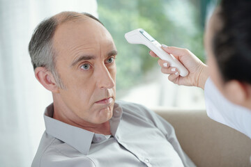 Doctor using non-contact infrared thermometer to check body temperature of senior patient