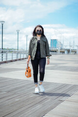 Naklejka premium Playing Ukulele of Young Beautiful Asian Woman Wearing Jacket And Black Jeans Posing Outdoors