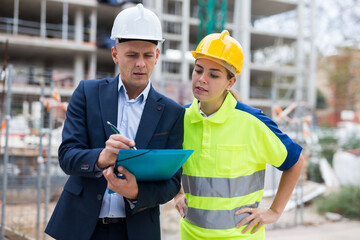 Engineer man in suit and hardhat planning work with employee woman in uniform in construction plant.