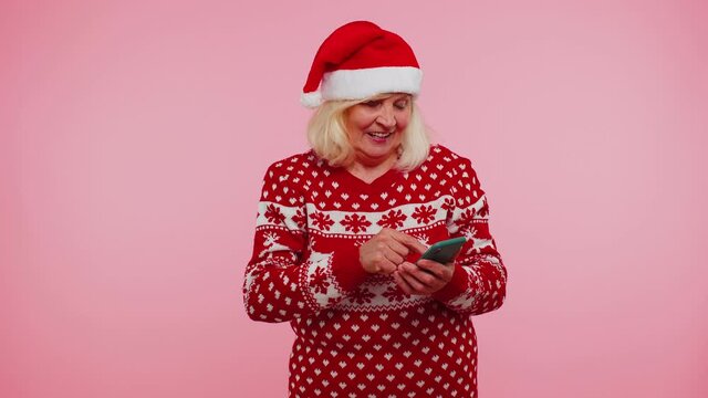 Grandmother in Christmas sweater using mobile phone typing new post on web, sms message, browsing, addiction of social networks. Blue background. Happy New Year celebration holidays shopping online
