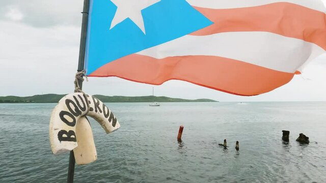Dolly forward shot along jetty overlooking sea rising up to a flag of Puerto Rico. Boqueron, PR.