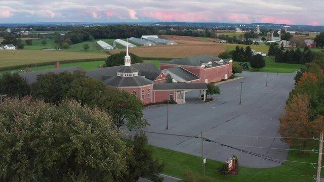Aerial of exterior, red brick Christian church and steeple in rural America. Cemetery, graveyard and parking lot. Front entrance portico.