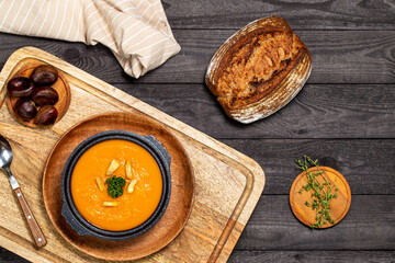 Pumpkin soup in black soup tureen aside entire chestnuts all on a board on a dark wood background with thyme twigs. Flat Lay.