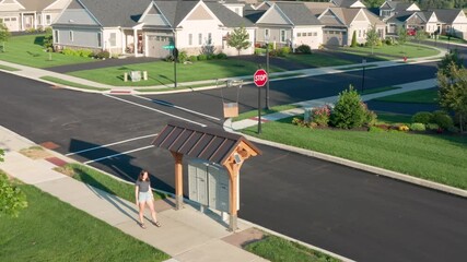 Female girl, woman accepts package box delivery from drone. Aerial follow shot in USA American neighborhood, beside mailboxes. Futuristic shipping logistics theme.