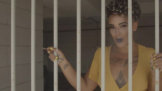 Yellow dressed Afro American Woman behind bars smoking and looking to the camera. Conceptual and metaphoric footage