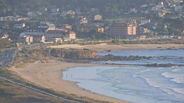 Static shot of La Lanzada beach, wooden path on the left with people walking and sea beach on the right, Galicia Spain