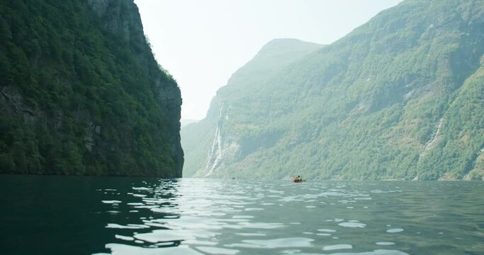 Pair paddle kayak in green fjord water along steep spectacular Geiranger cliffs