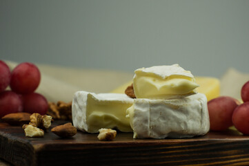 Camembert cheese is the most famous French cheese on a wooden board with nuts and grapes. closeup.