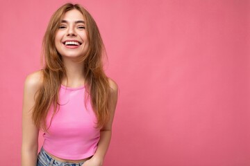Obraz na płótnie Canvas Emotional happy young charming dark blonde woman with sincere emotions isolated on background wall with copy space wearing stylish pink top. Positive concept