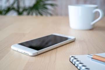 テーブルの上に置かれたスマホ、ノート、ペン、コーヒーカップ