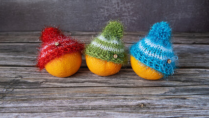 Three mandarins in knitted Christmas hats on a wooden background