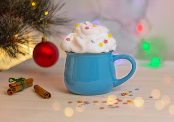 beautiful festive drink with whipped cream in blue cup near christmas tree