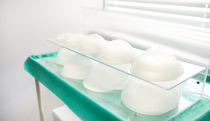 Fototapeta na wymiar Medical sample of silicone implants of various shapes and sizes for breast augmentation on glass surface in plastic surgery clinic. Mammoplasty concept, breast reshaping after breast resection surgery