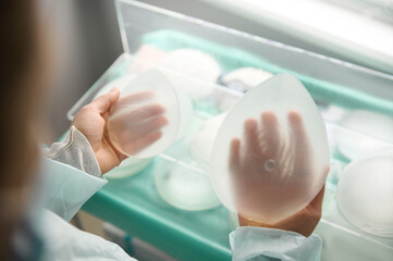 Overhead view of silicone breast implants prosthesis of various sizes in plastic surgeon hands, for...