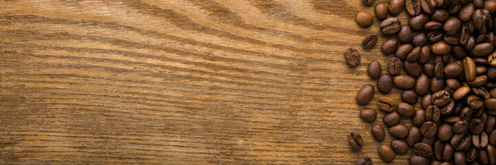 Fresh brown coffee beans on dark wooden table background. Closeup. Empty place for text. Wide banner. Top down view.