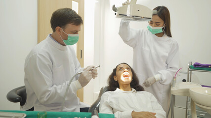 A dentist checking up a woman patient's teeth by using dental mouth mirror at hospital clinic....