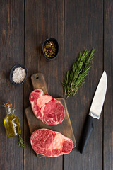 Two fresh raw steaks of osso buco meat on wooden cut board with condiments and knife. Ingredients for  cooking