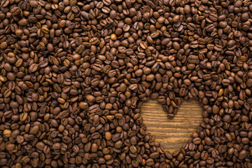 Small heart shape created from fresh dark brown coffee beans. Empty place for text. Closeup. Top down view.