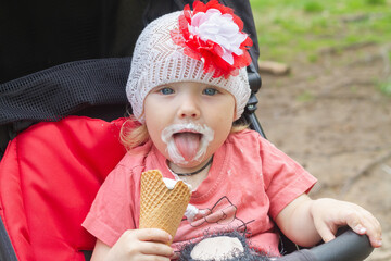 Baby girl licks ice cream with her tongue on a hot summer day
