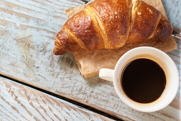 Morning croissant and a cup of coffee on a wooden background