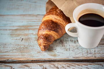 Morning croissant and a cup of coffee on a wooden background