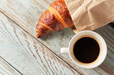 Morning croissant and a cup of coffee on a wooden background
