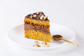A slice of pumpkin pie with chocolate ganache, orange confit and nuts on a white plate. Sugar, gluten and lactose free, vegan.