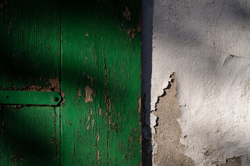 Wooden door of an old Farmhouse in Arnsberg Sauerland Germany. Close up details of green door, hinge and wheathered white wall of a barn stable lit by low sunlight. Rural agriculture background. 