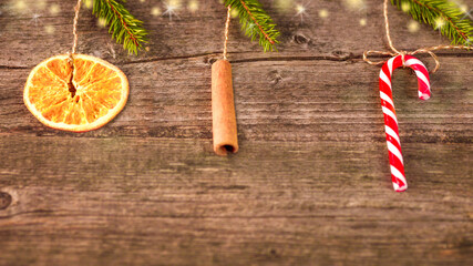 Circle of dried orange, a stick of cinnamon, a striped red lollipop with branches of a Christmas tree on an old wooden background. 