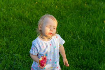 Baby girl is resting on the lawn on a hot summer day and eating a sweet donut