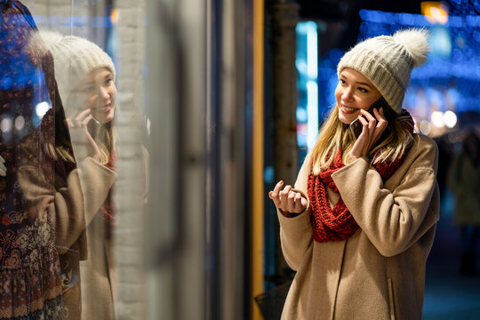 Portrait of beautiful happy young woman calling on smartphone over christmas light in winter evening