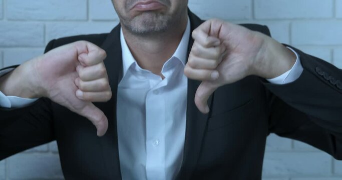 Negative thumb sign. A man negatively show his thumb dowm in the office.