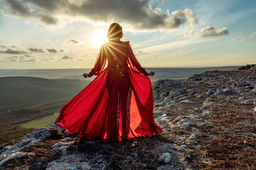 Rise of the mystic. sunset over the clouds with a girl in a long red dress. Stands on the mountain with a magical view.