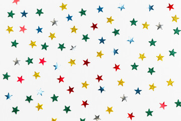 White background with colored sequins in the shape of stars. Festive backdrop for your projects. Background for your product presentation. Christmas texture. Top view, copy space.