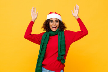 Surprised woman in Christmas attire smiling and raising hands up in yellow studio isolated background