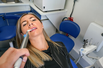 Young woman posing with her mouth half open at dentist chair, dental tool near her teeth, first person view