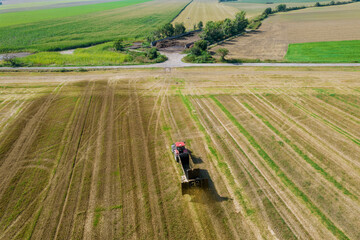 A red tractor from a trailer scatters manure on a field near a farm. Solid organic fertilizers. View from above.