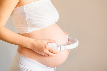 pregnant woman holding white headphones near her belly, toddler listening to music