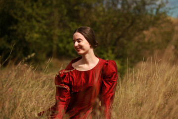 Young woman in vintage red dress sitting on a grass in a valley