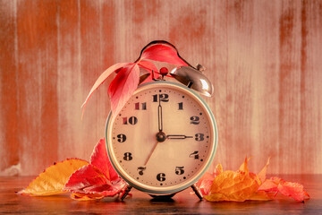 Daylight Savings Time concept, fall back in autumn, toned image. A vintage alarm clock with autumn leaves on a rustic wooden background