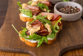 Bruschetta with prosciutto and arugula on a wooden board. Smoked meat