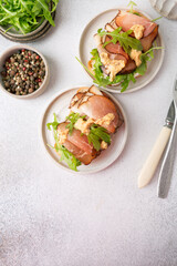 Bruschetta with prosciutto and arugula on a plate. Light background