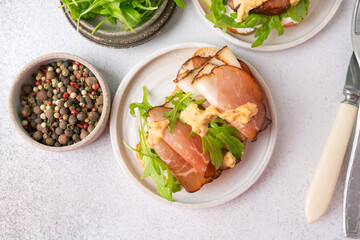 Bruschetta with prosciutto and arugula on a plate. Light background
