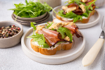 Bruschetta with prosciutto and arugula on a plate. Light background