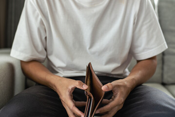 Young man wearing white t-shirt sitting on sofa and holding empty wallet. He was worried that he had no savings and no financial planning.