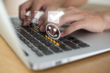 Businesswoman pressing face emoticon on the laptop and selecting smiley face icon and a 5 star rating. Demonstrates that customer satisfaction is essential to a successful business.