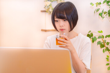 グラスを片手にパソコンを見つめる女性