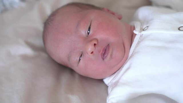 Beautiful little newborn laying on white blanket. Close up view of small cute baby in light cloth.